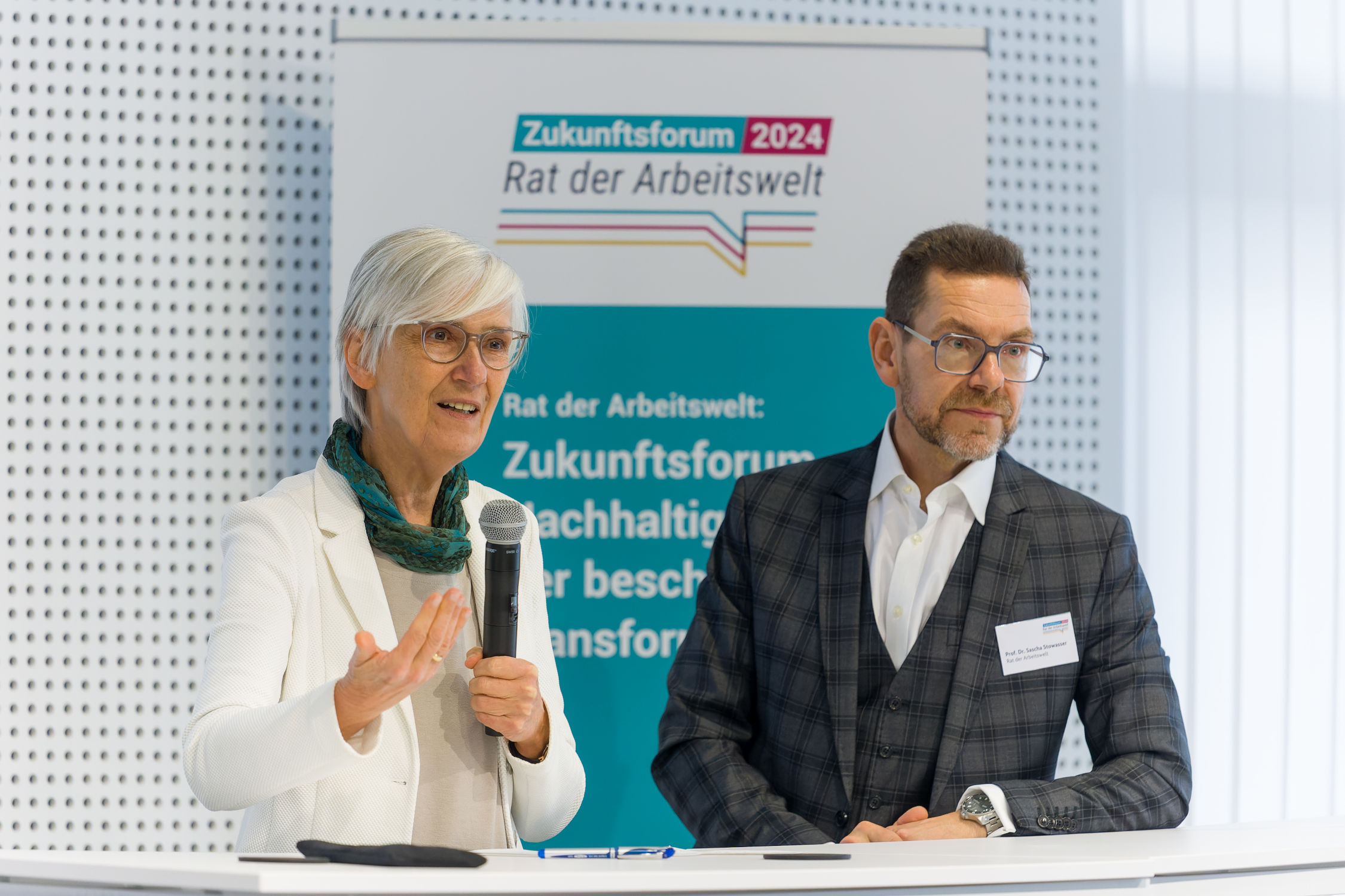Isabel Rothe spricht mit Mikrofon. Prof. Dr. Sascha Stowasser steht neben ihr